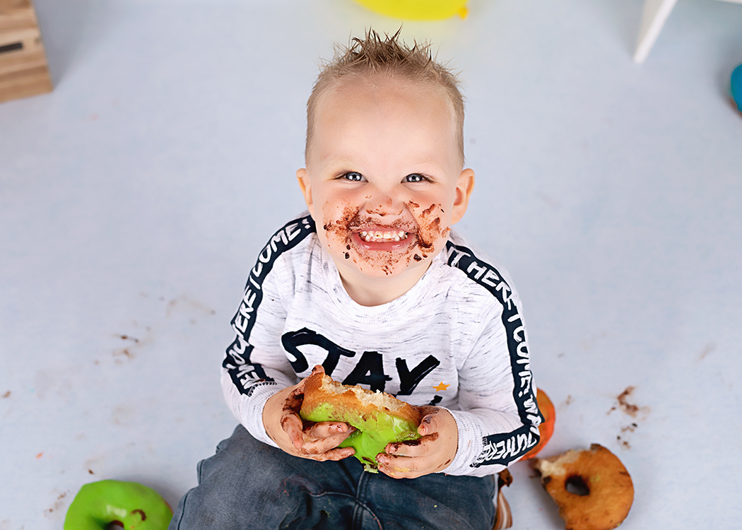 jongen lacht in camera met donut in zijn hand